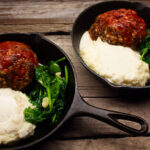 two sperate iron skillets with a meatloaf dinner in each