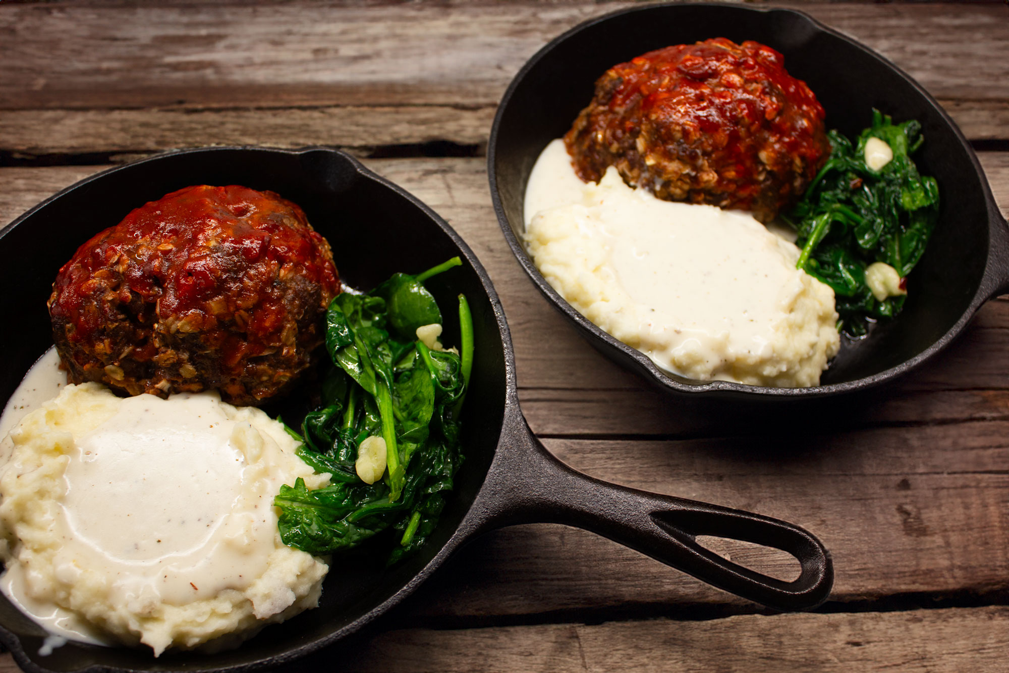two sperate iron skillets with a meatloaf dinner in each